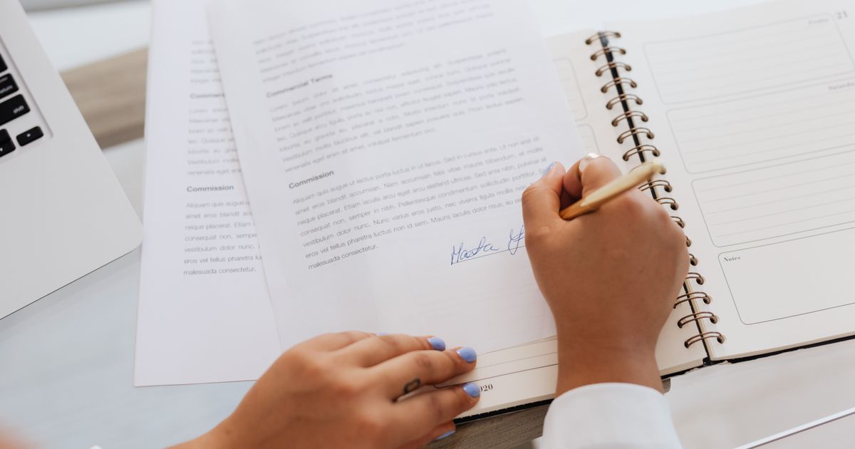 ノートに書類を確認しながらサインする手元(イメージ)